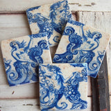 Four square ceramic coasters with a blue and white mermaid pattern, arranged on a rustic white-painted wooden surface.