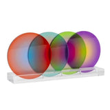 Four overlapping translucent circular coasters in red, blue, green, and purple hues, displayed on a clear acrylic stand against a white background.