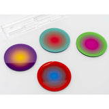 Four circular gradient color coasters in purple/yellow, teal/red, green/magenta, and red/blue, arranged on a white background with a clear plastic base partially visible in the upper left.