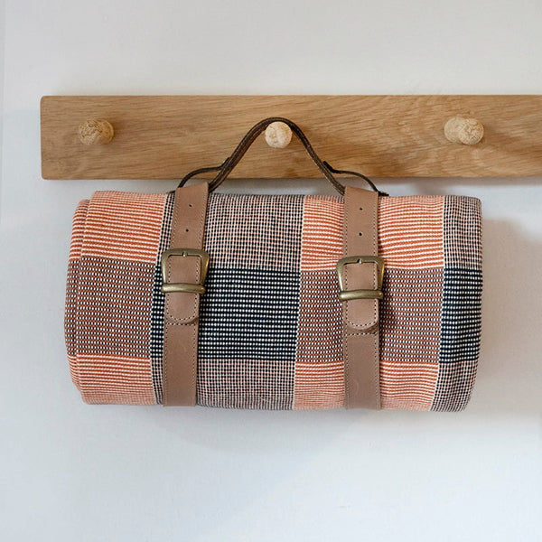 Woven bag with leather straps hanging on a wooden rack against a white wall.