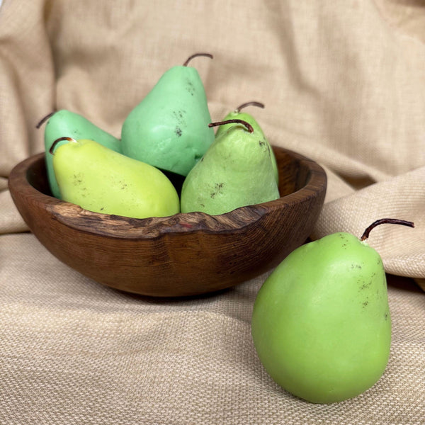Pear shaped candles in a wooden bowl on a tan background