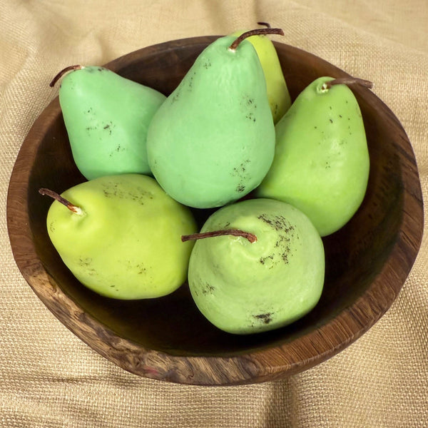 Pear shaped candles in a wooden bowl on a tan background
