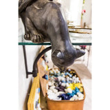 Bronze finish resin statue of a cat with a bowl of multicolored stones on a glass shelf.
