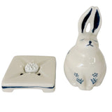 A white ceramic rabbit figurine with blue painted details, sitting next to a matching rectangular base against a plain white background.