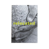 A book cover featuring a black-and-white close-up of a hand resting on a rough stone, with the word 'relocated' in bright yellow across the center, displayed against a white background.
