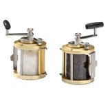 Two brass and stainless steel manual grinders side by side on a white background, one filled with coarse white salt and the other with whole black peppercorns.