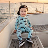 Child on a boat wearing a light blue outfit with ship pattern and black sneakers.