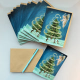 A set of Christmas greeting cards and matching kraft envelopes arranged on a white surface. The cards feature an illustration of a glowing Christmas tree with a small faerie in the sky above.