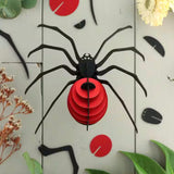 Black spider-shaped decoration with a red center on a light wooden background with flowers and leaves.