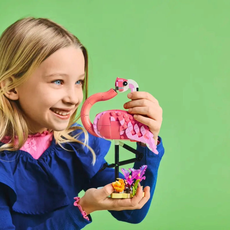 Young girl holding a pink flamingo toy made of interlocking bricks against a green background
