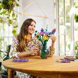 Woman arranging LEGO flowers in a vase at a table with a bright, natural light setting.