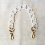 White chain strap with gold clasps on a light beige background