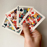 Hand holding three playing cards with colorful designs on a plain background