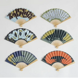 Six folding hand fans arranged in two columns of three on a plain white background. Each fan has a different Japanese-style printed design featuring snakes, stripes, and patterns in muted colors including brown, green, blue, orange, and black.