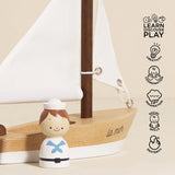 Small figurine of a child in a sailor outfit next to a wooden sailboat model with educational icons on a beige background.