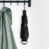 Black umbrella hanging on a hook next to a green jacket on a white background