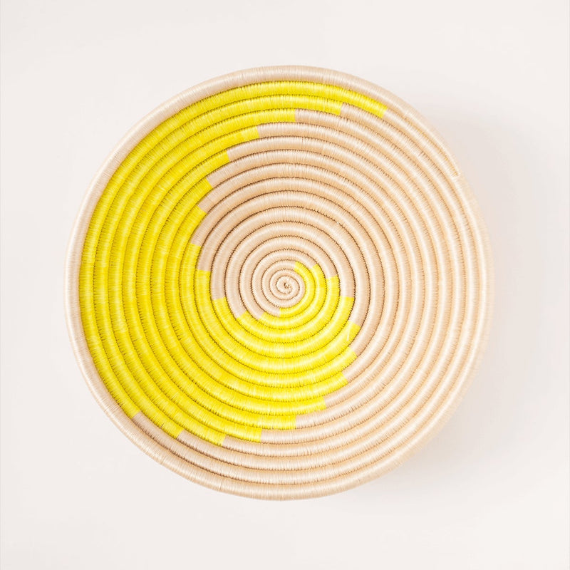 Round woven basket with yellow and beige spiral pattern on a white background