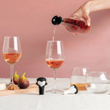 Person pouring rose wine into a glass with a pink background, surrounded by wine glasses and figs.