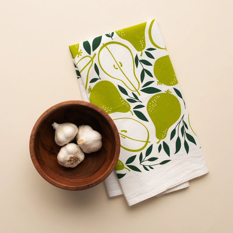 Dish towel with pear pattern next to a wooden bowl with garlic on a beige background