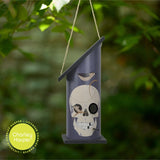 Decorative birdhouse with skull design hanging against a blurred green background