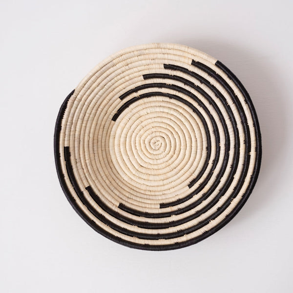Woven basket with concentric black and beige circles on a light gray background
