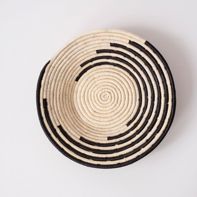 Woven basket with concentric black and beige circles on a light gray background