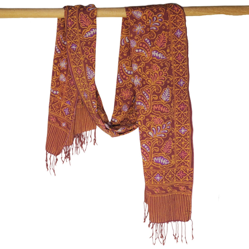 Patterned scarf with fringes hanging on a wooden rod against a white background