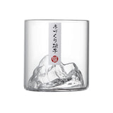 A clear glass cup featuring a sculpted mountain design at the base and a vertical white label with black Japanese text and a small red seal.
