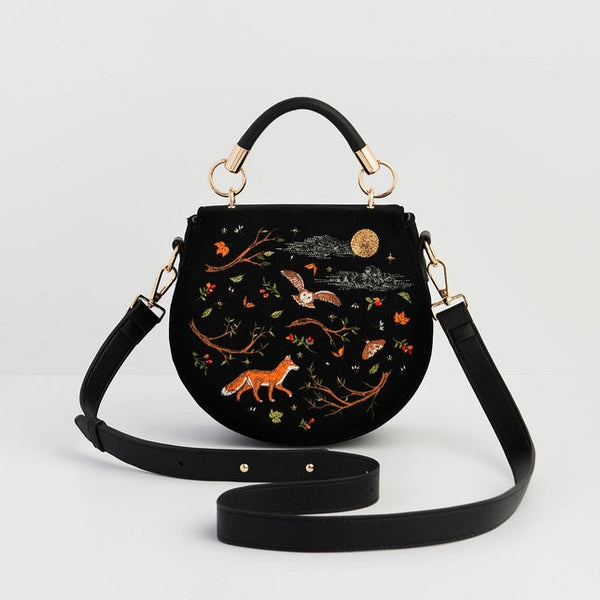 Black handbag with embroidered designs on a light gray background