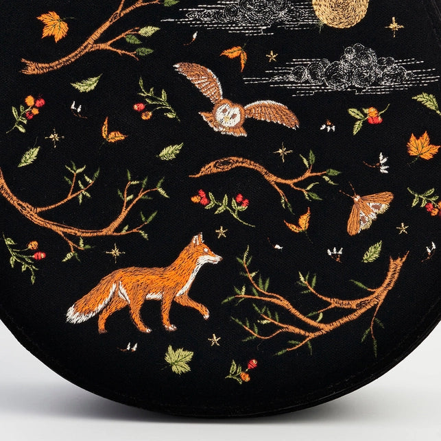 Embroidered design of a fox, owl, and branches on a black background