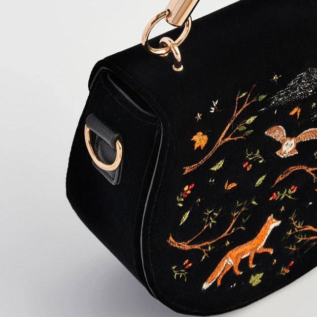 Black handbag with fox and nature-themed embroidery on a light gray background