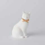 White ceramic cat figurine with a gold ribbon on a light gray background