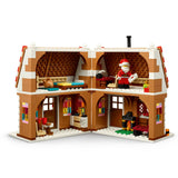 A LEGO-style multi-level house building set shown open on a white background, with brown and cream brick walls, interior rooms, small furniture pieces, and a Santa minifigure standing inside the upper right room.