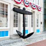 A large black anchor, displayed outdoors in front of a historic building with red, white, and blue patriotic bunting.