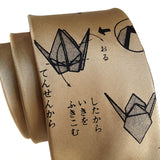 A gold-colored necktie featuring a black origami crane pattern with Japanese instructions and text printed on it, shown against a plain white background.