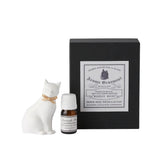 Small bottle of essential oil, white cat figurine, and black box with decorative label on a white background